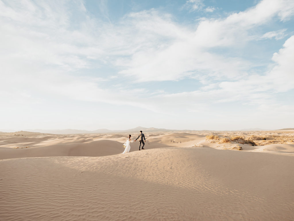 Bride and groom walk across sand dunes