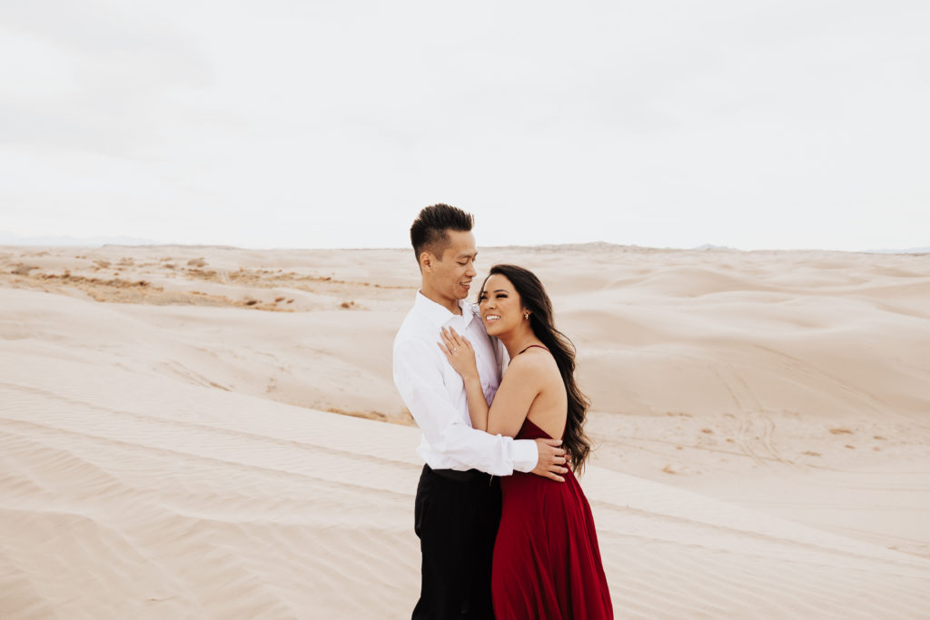 man picks up girl in red dress in little sahara sand dunes