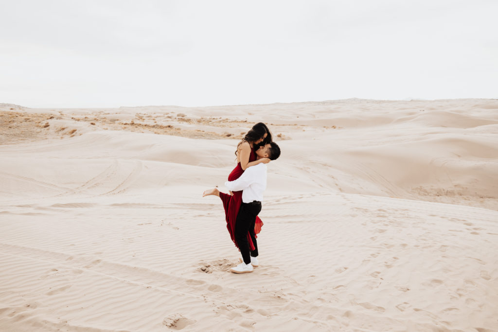 man picks up girl in red dress in little sahara sand dunes photos
