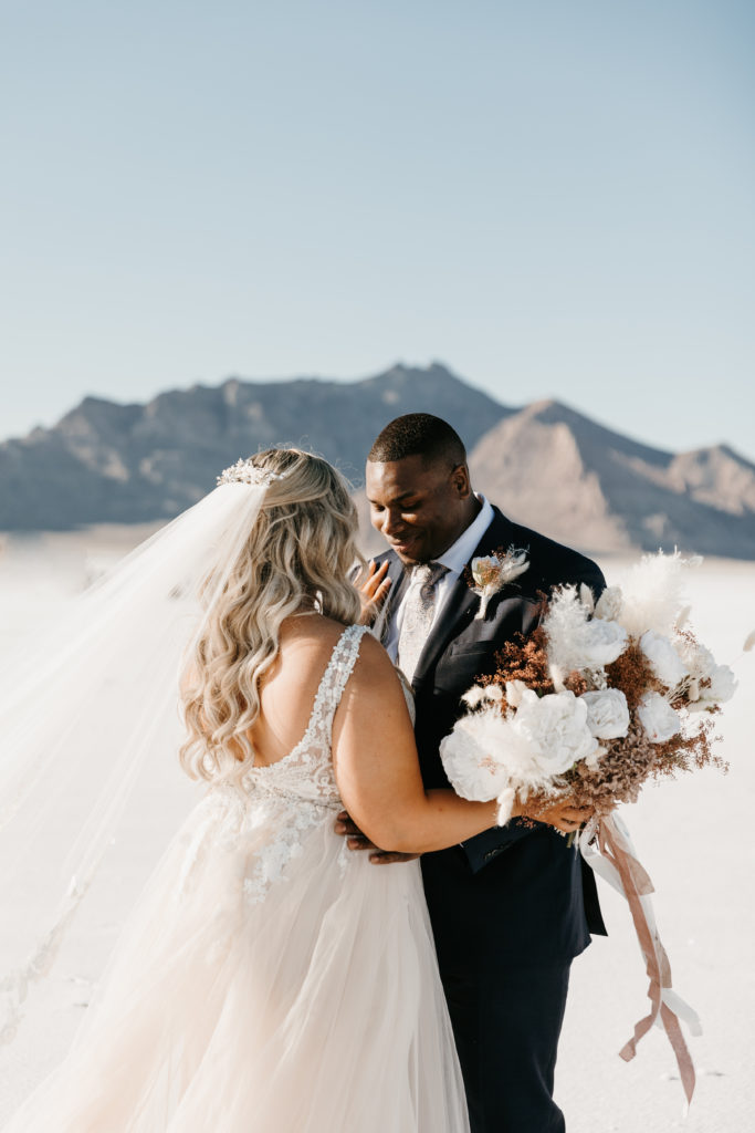 bride and groom have a first look in utah salt flats blue mountains
